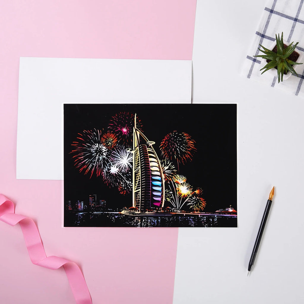 Scratch art kit featuring a colourful skyscraper with fireworks at night, displayed with a stylus on a pink background.