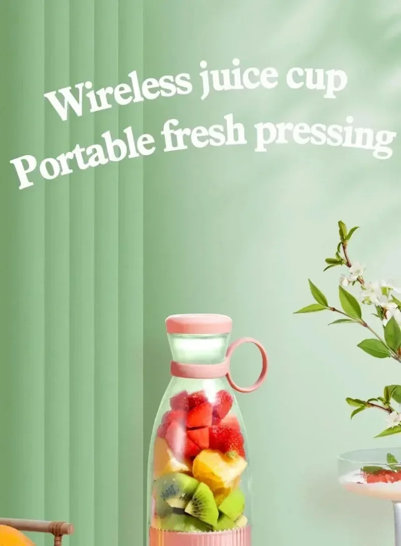 A portable wireless juice blender in pastel pink with a clear cup filled with chopped fruit on a green background.