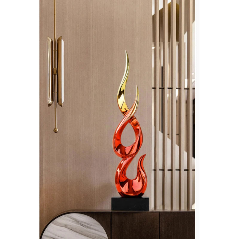 Modern abstract flame sculpture in glossy red and gold resin on a black base, standing on a dark wooden cabinet.