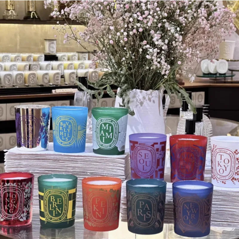 Assorted colourful glass scented candles, each featuring unique city-themed labels and designs on display.