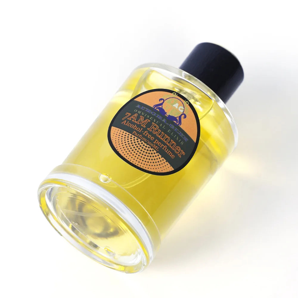A clear glass bottle of yellow, alcohol-free perfume with a black cap and a round orange and black product label.