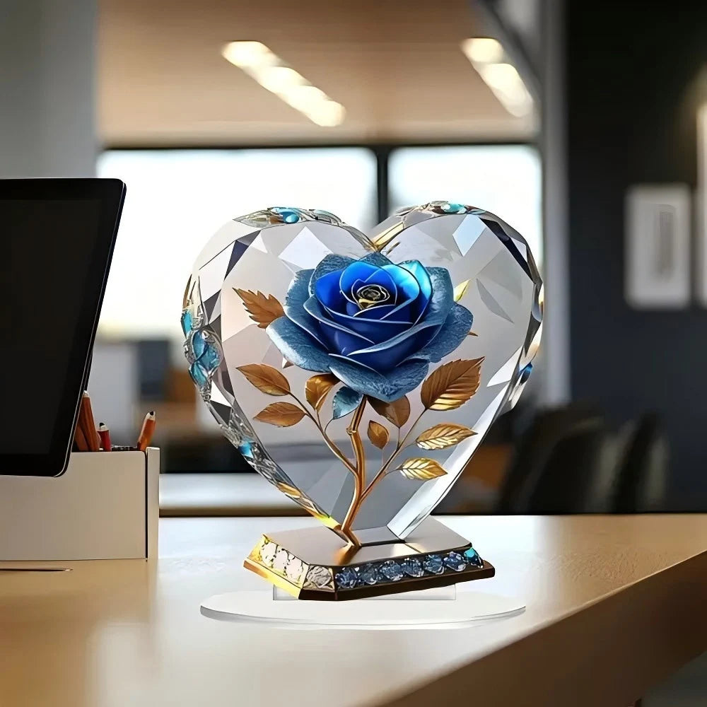 A heart-shaped clear acrylic ornament featuring an elegant blue rose with gold stems and leaves on a decorative base.