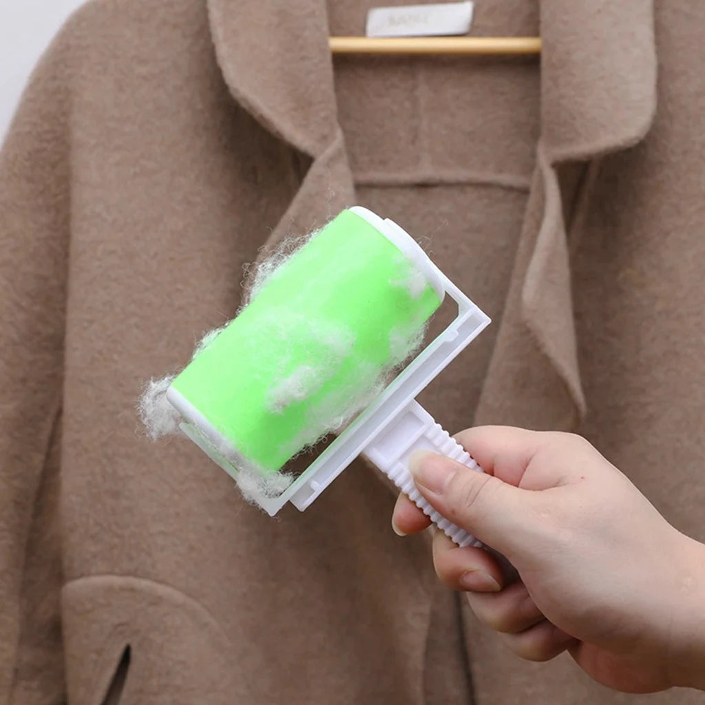 Hand holding a bright green lint roller covered in white fluff, positioned against a brown wool coat on a hanger.