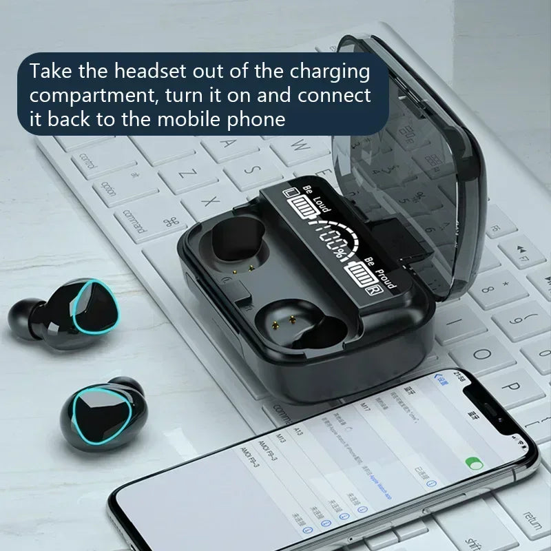 Black wireless earbuds with a charging case featuring a digital battery display, sitting on a keyboard near a phone.