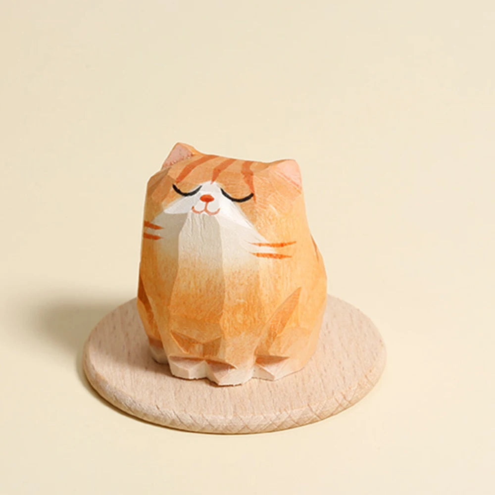 Small, carved wooden orange tabby cat figurine with closed eyes, perched on a circular wooden base.