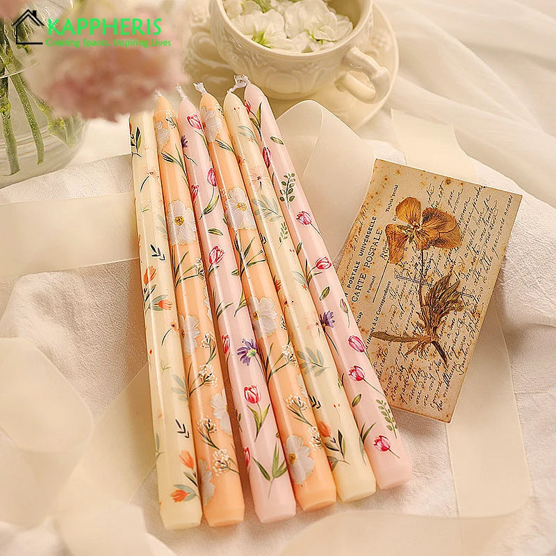Set of five tapered candles in pastel peach, pink, and cream, decorated with delicate floral and botanical prints.