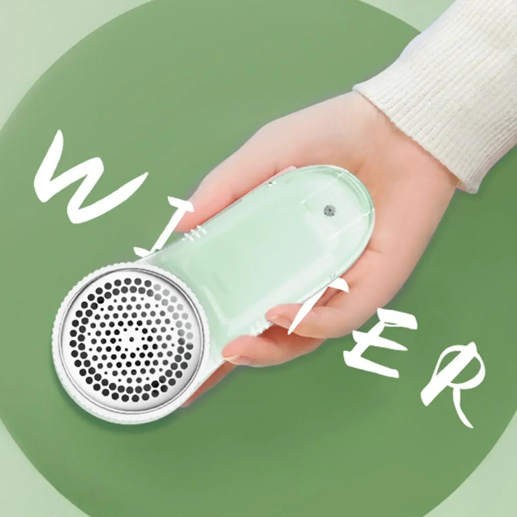 Hand holding a pastel green fabric bobble remover with a metallic mesh head against a green background.