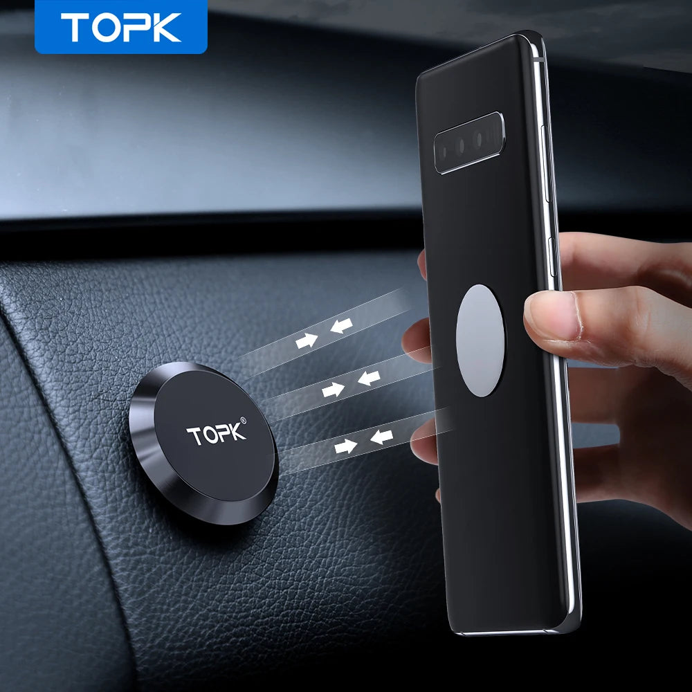 A small, circular black magnetic car phone mount attached to a dashboard, with a smartphone being held up to it.