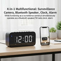 Black plastic digital alarm clock with a built-in camera, Bluetooth speaker, and FM radio on a desk.