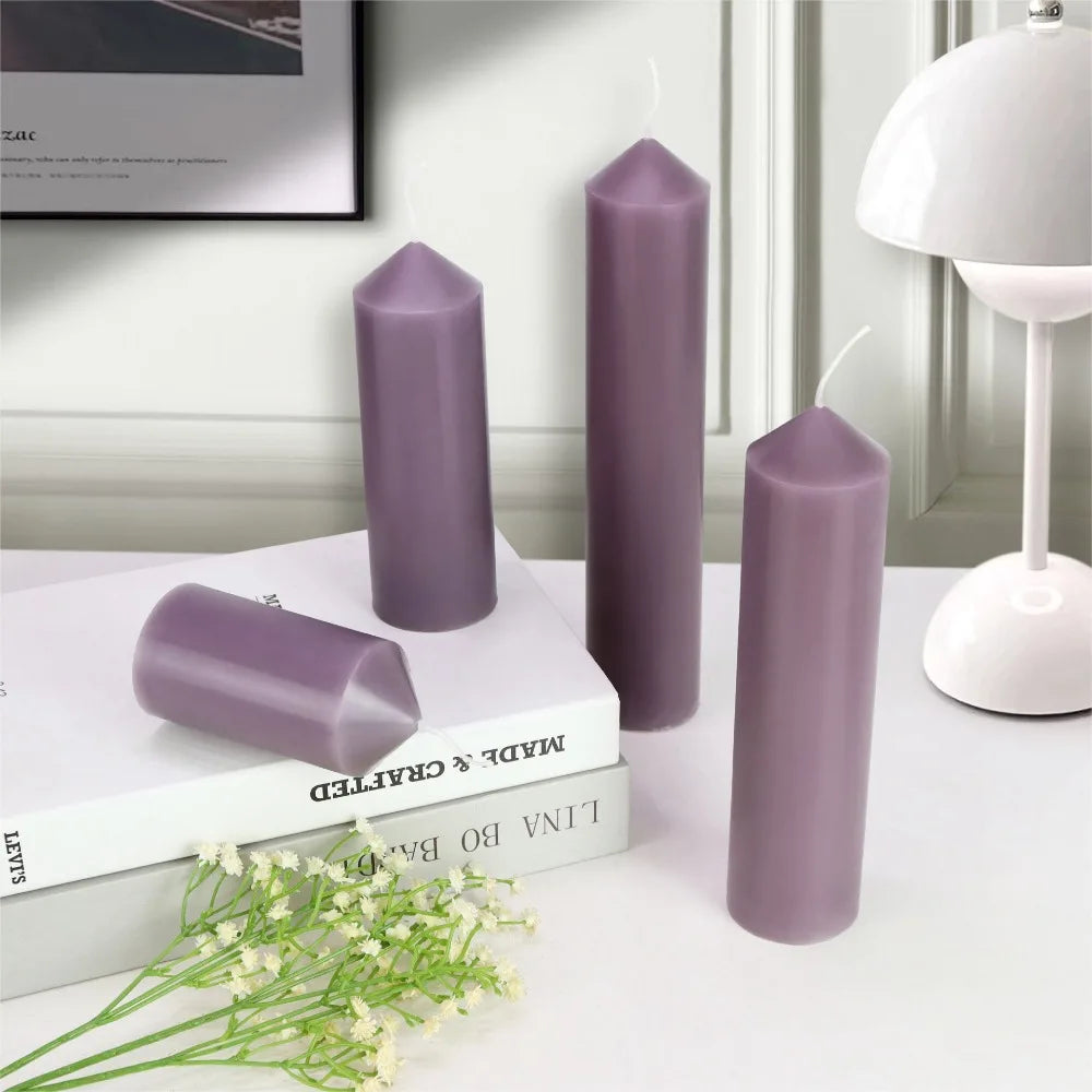 Four purple taper cylinder candles in varied heights with pointed tops on books next to a white lamp.
