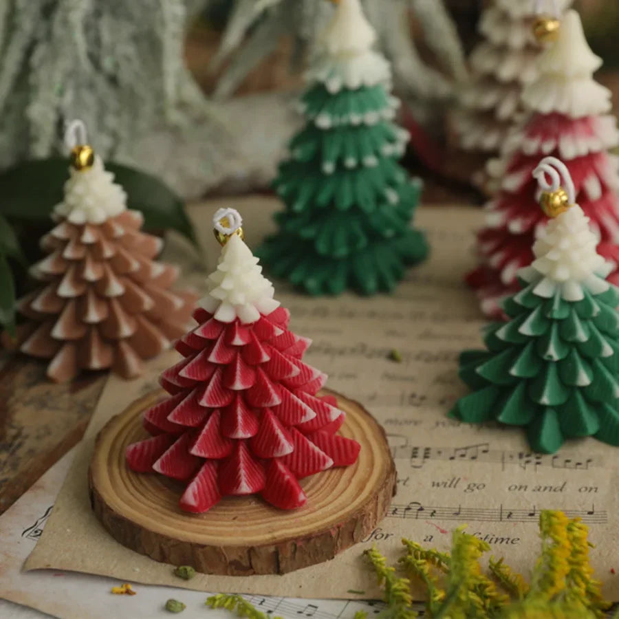 Assorted miniature Christmas tree-shaped candles in red, green, and brown with snowy tips on a rustic wooden coaster.