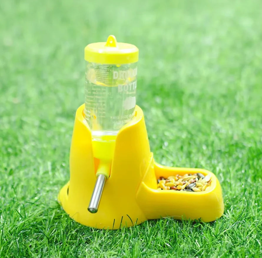 Yellow pet feeder and water bottle combo with metal spout on a grass background.