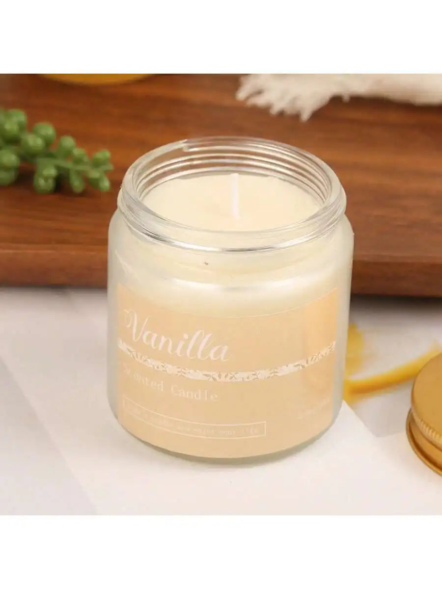 Vanilla scented candle in a clear glass jar with a cream label and gold lid on a wooden background.