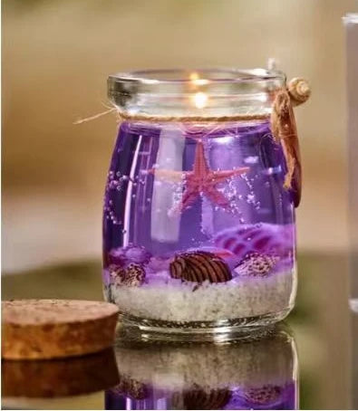 Purple gel candle in a glass jar featuring starfish, seashells, and sand, tied with twine and a decorative shell.