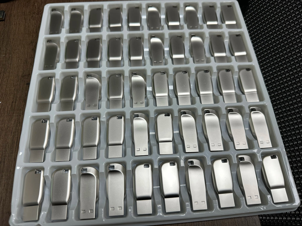 A bulk tray of sleek, silver-toned metal USB 3.0 flash drives with a minimalist, smooth contoured design.