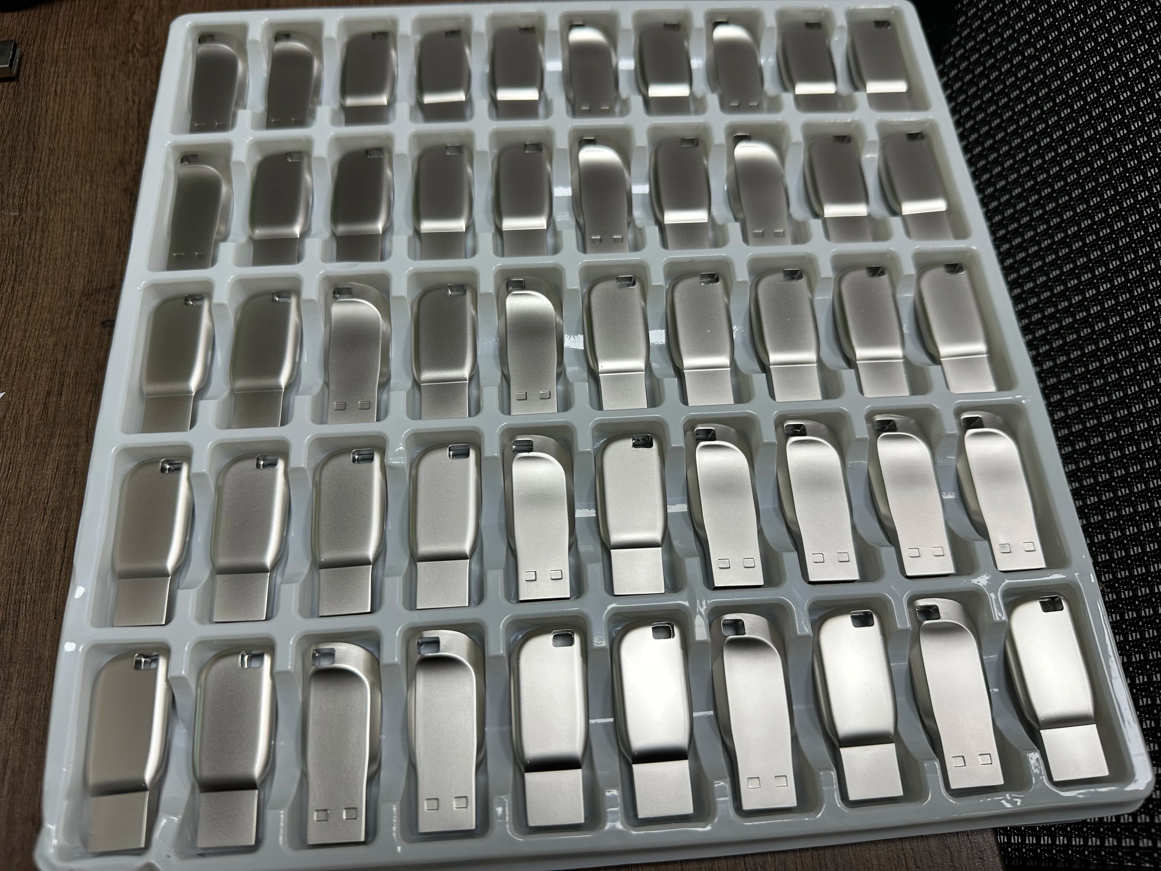 A bulk tray of sleek, silver-toned metal USB 3.0 flash drives with a minimalist, smooth contoured design.