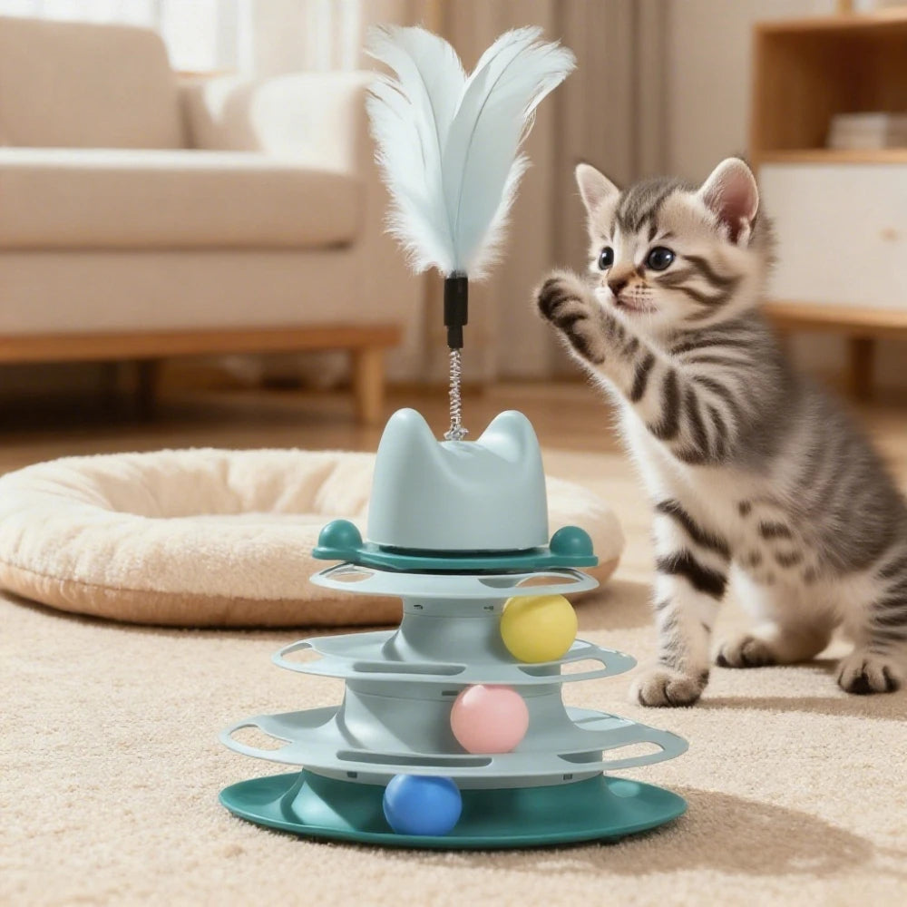 A cute tabby kitten playing with a mint-green, tiered cat turntable featuring rolling balls and a feather teaser wand.