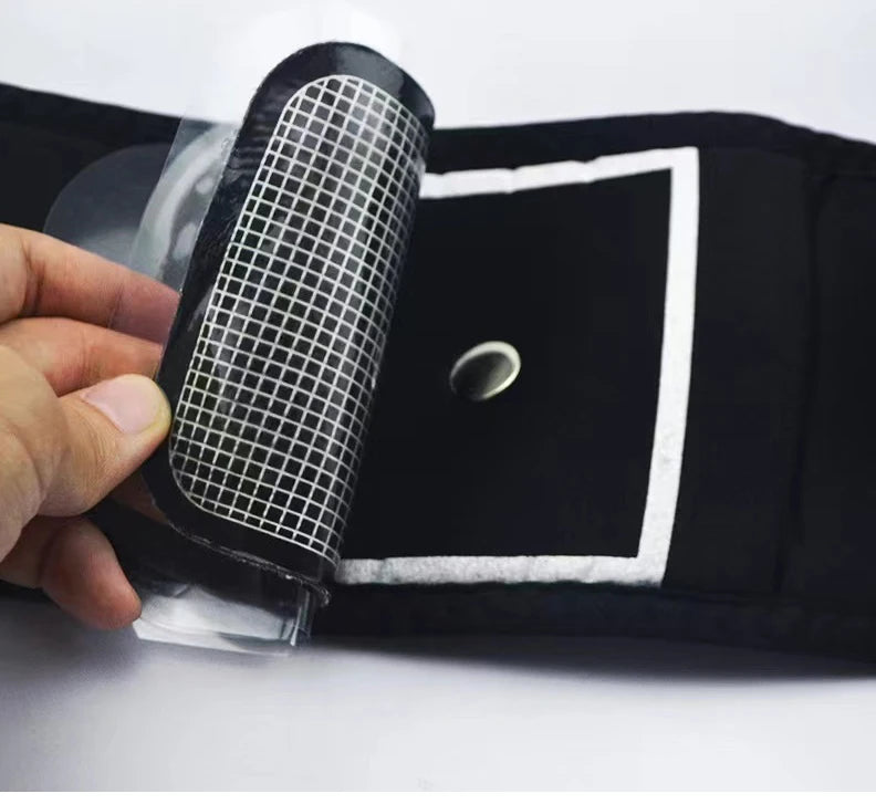 Close-up of a black abdominal fitness belt with a peel-back grid adhesive pad and a central metal contact stud.