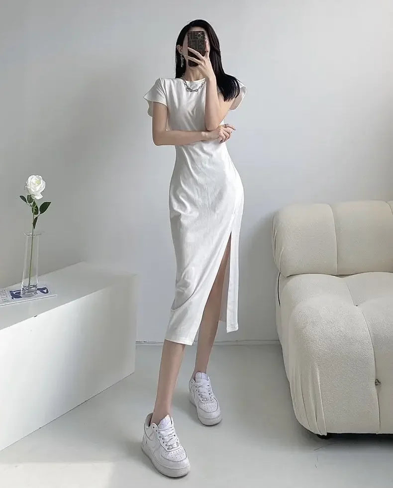 Woman wearing a short-sleeved white midi dress with a high side slit, paired with white trainers.
