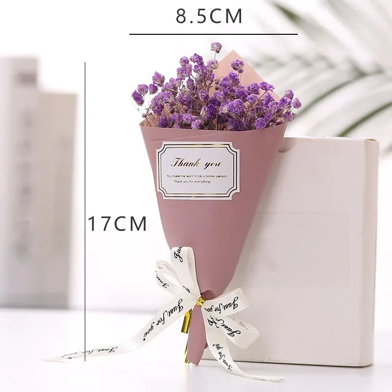 Small bouquet of purple artificial flowers wrapped in dusty pink paper with a 'Thank you' label and white ribbon.