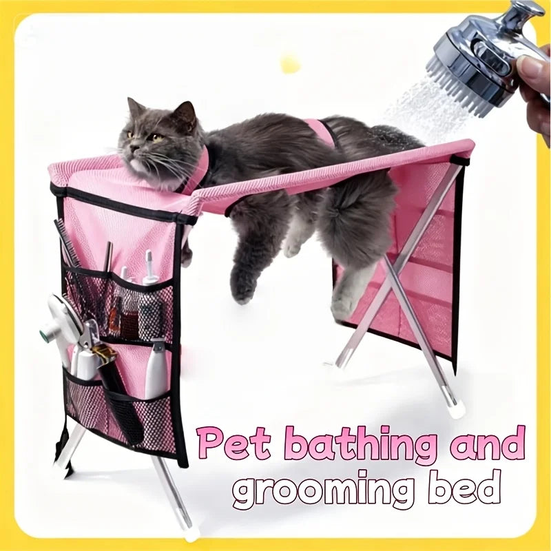 Pink foldable pet grooming table with a hammock top, mesh storage pockets, and a cat resting inside.