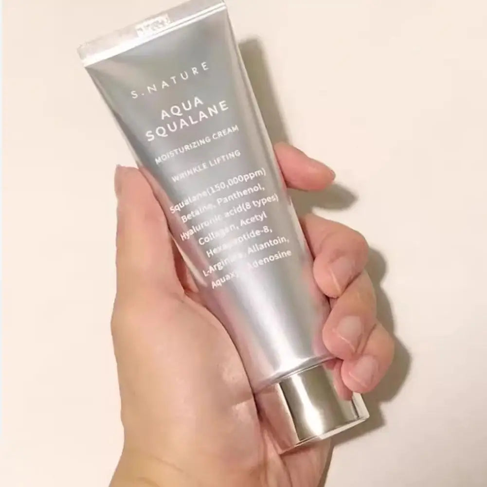 A hand holding a silver tube of Aqua Squalane moisturizing cream, featuring wrinkle-lifting and collagen ingredients.
