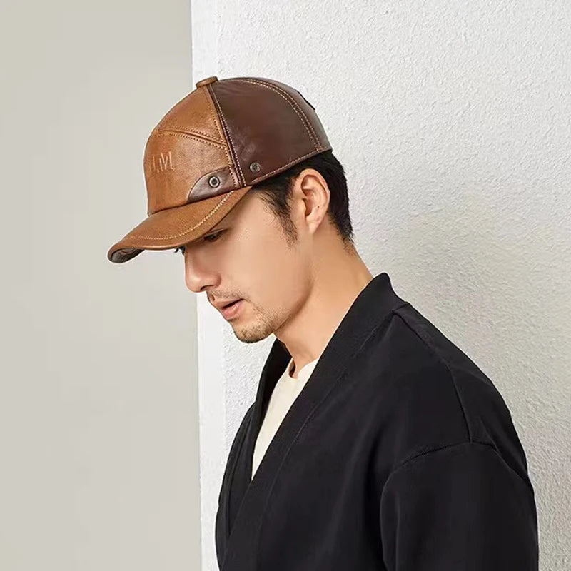 A man wearing a two-tone brown genuine leather baseball cap with fold-down ear flaps and press-stud detail.