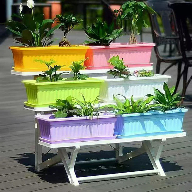 A tiered white stand holding colorful rectangular plastic plant pots with various green indoor plants on a deck.