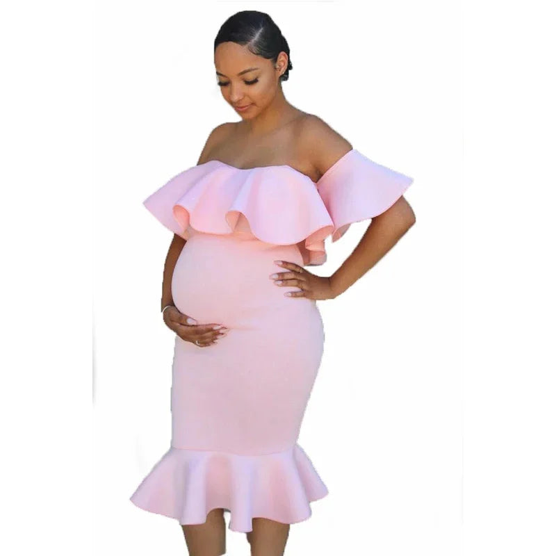 Pregnant woman in a pale pink off-the-shoulder maternity dress with ruffled neckline and fishtail hem.