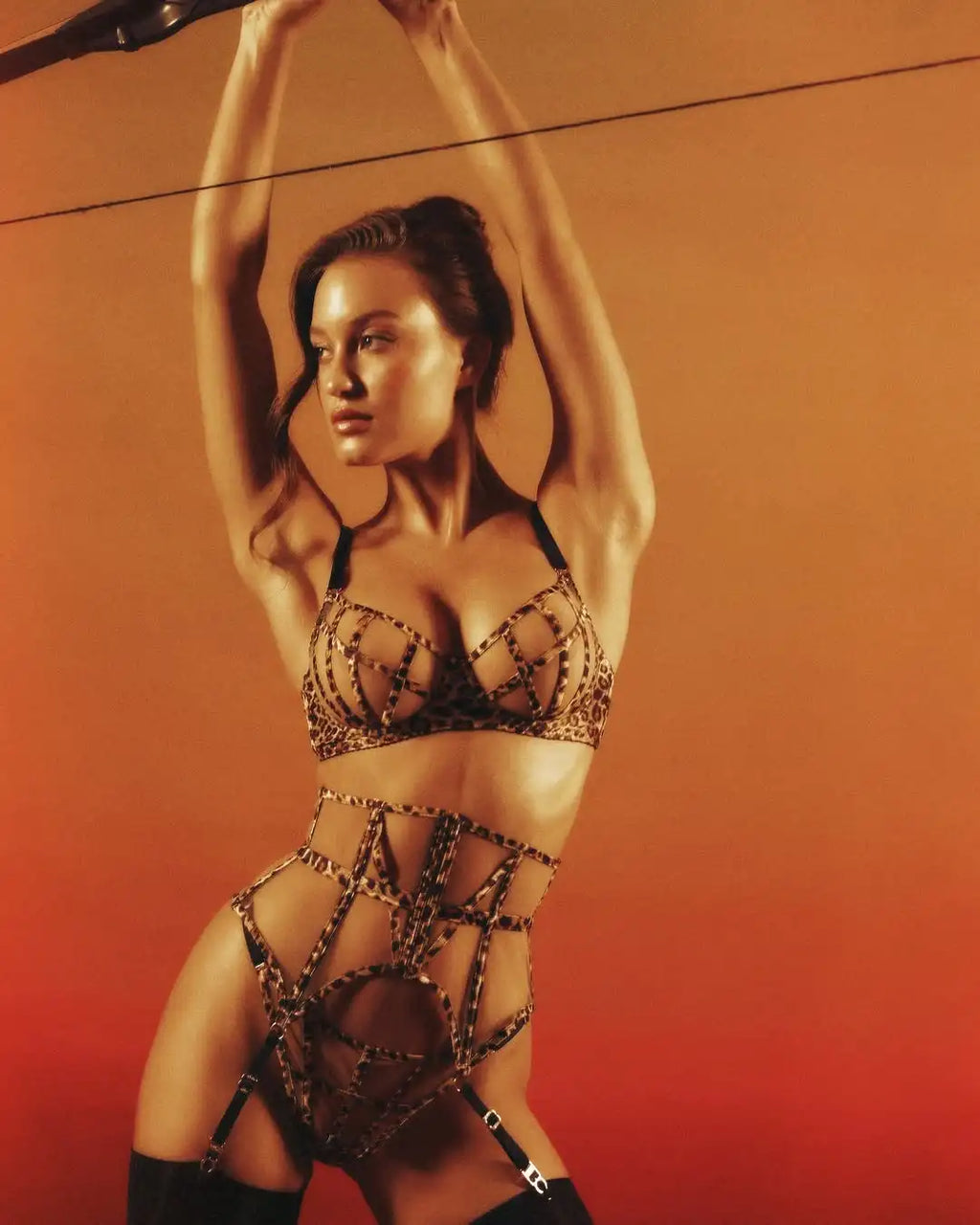 Model in a luxury leopard print bra and strappy high-waisted underwear set with black thigh-high stockings.
