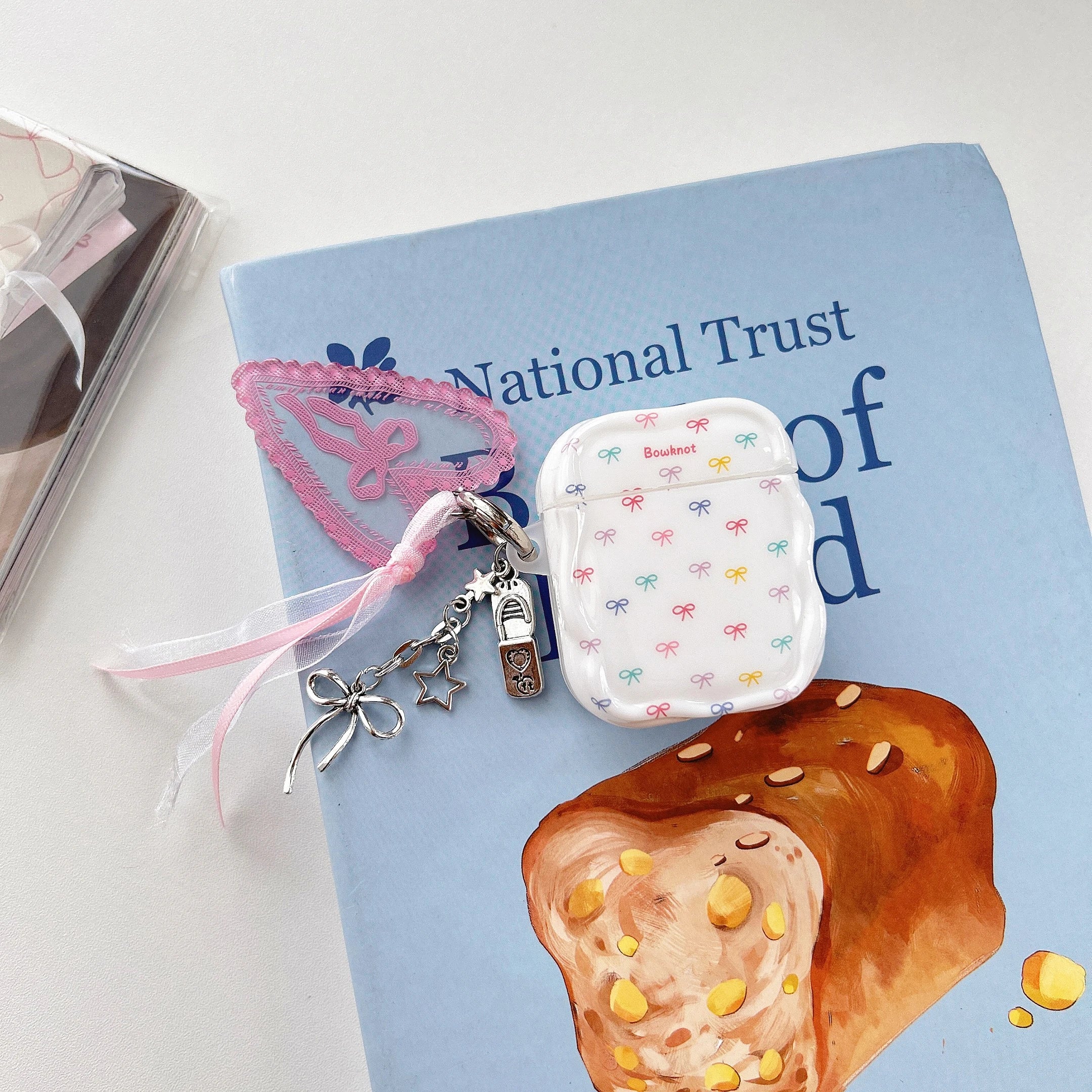 Clear AirPods case with colourful bow pattern and decorative ribbon and charm keychain. Fits standard AirPods.