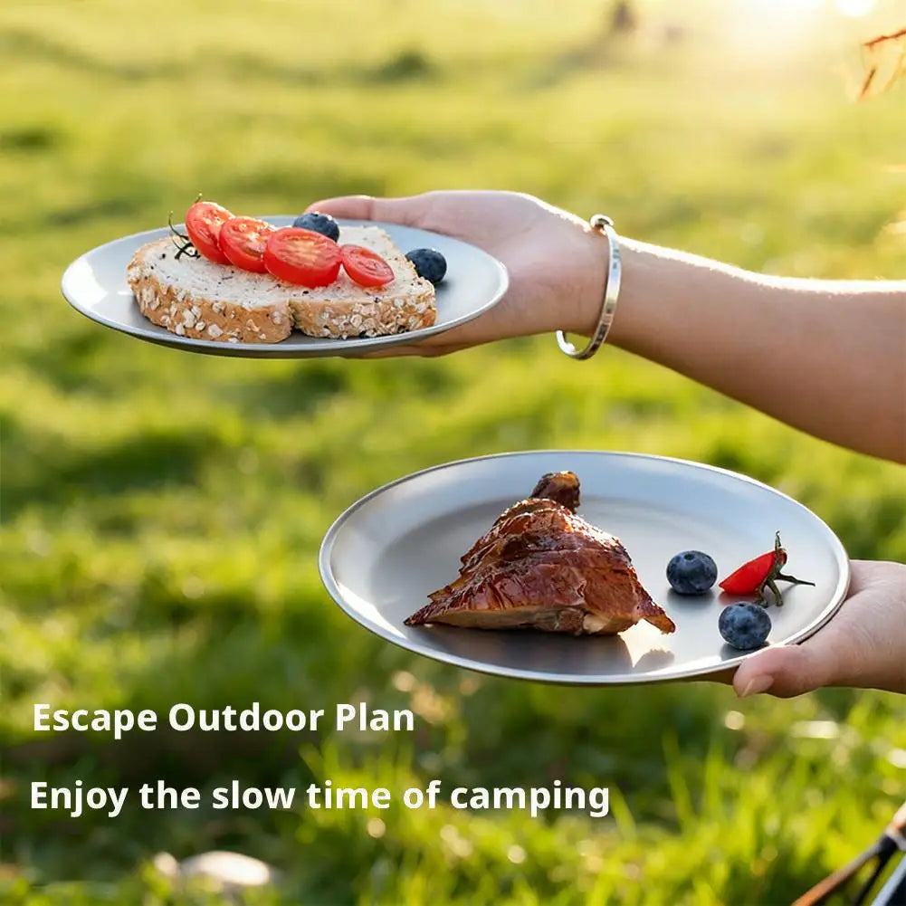 Two titanium plates with food held outdoors against a grassy backdrop.