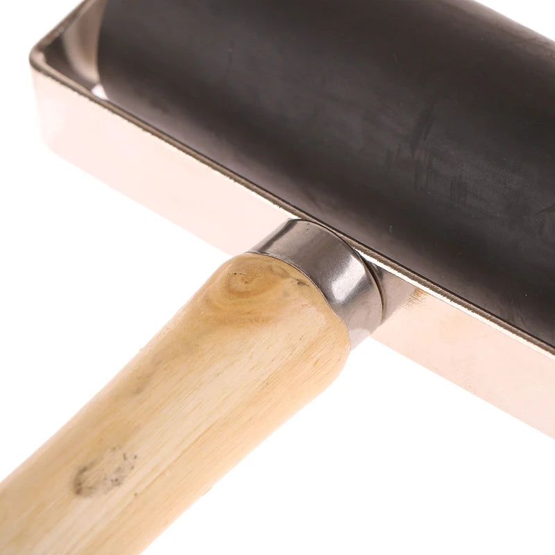Close-up of a rubber craft brayer roller with a black barrel, metal frame, and natural wood handle.