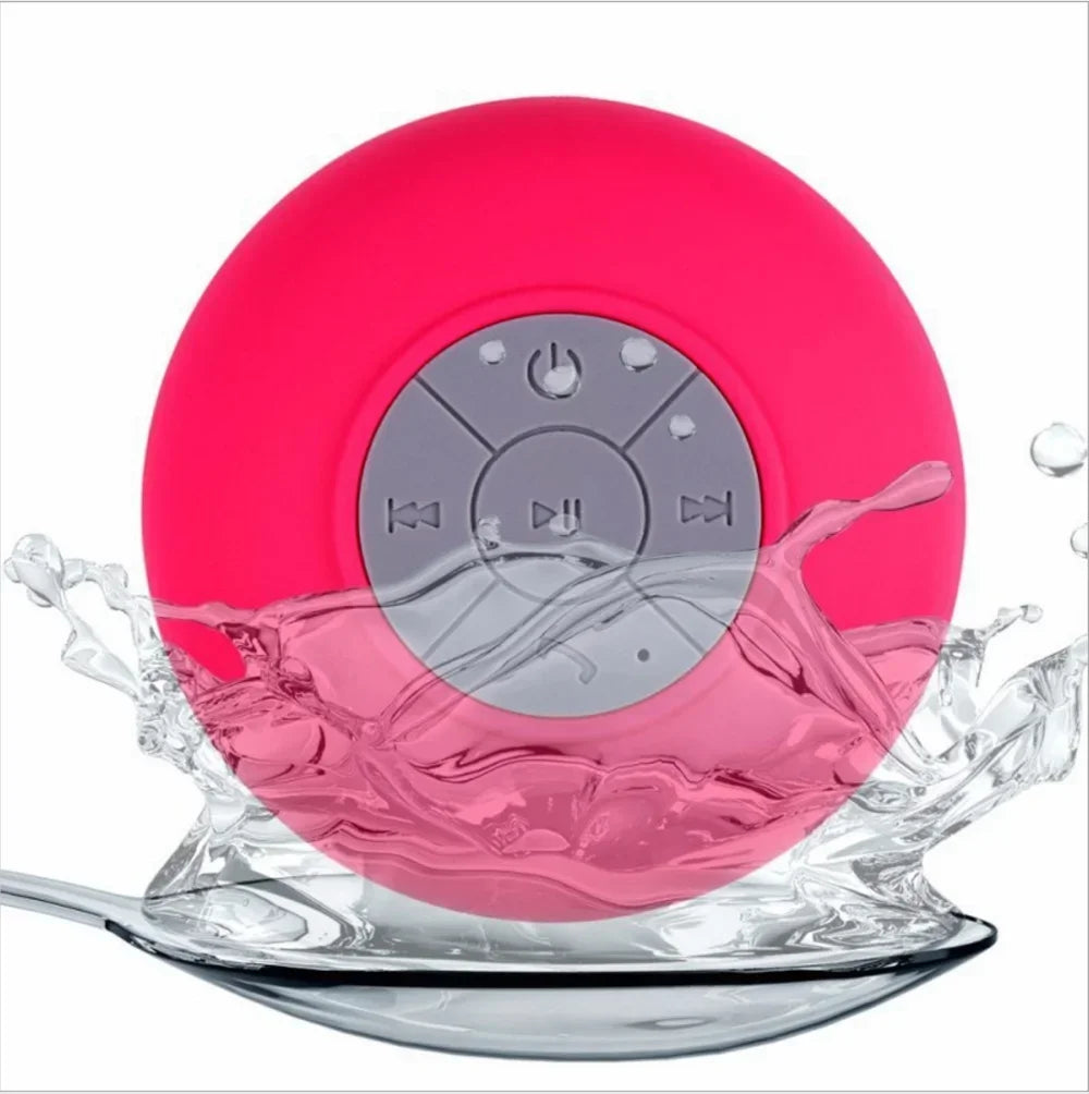 Bright pink, round wireless waterproof speaker with a grey control panel and suction cup, surrounded by water splashes.