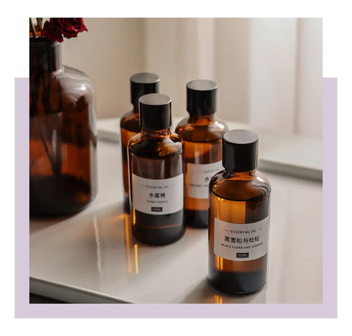 Four amber glass essential oil bottles with black screw-top lids and minimalist white labels, set on a white tray.