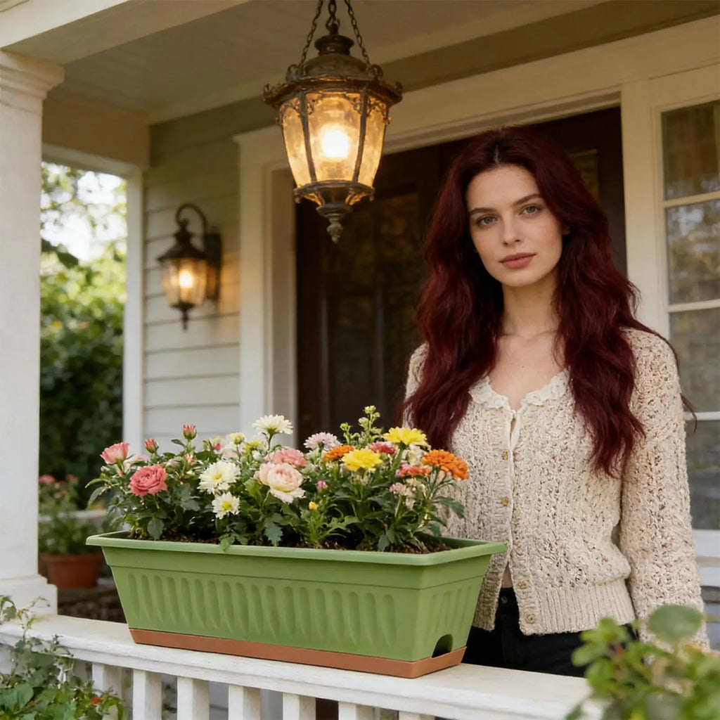 A woman holds a rectangular, sage-green plastic planter filled with colorful flowers on a white porch railing.