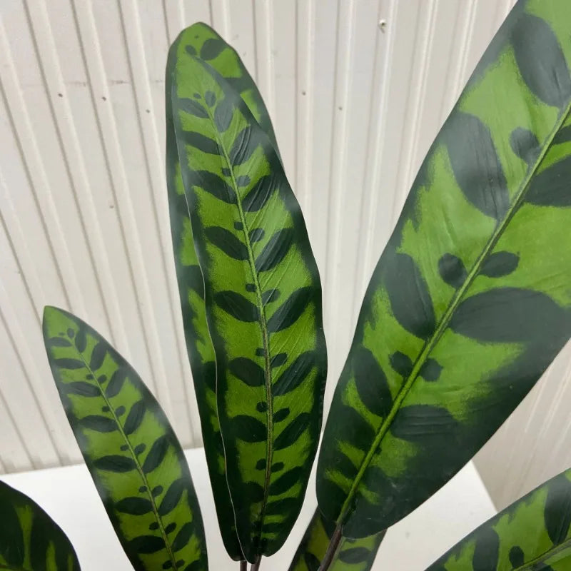 Artificial plant with long, lance-shaped green leaves featuring dark, patterned spot designs.