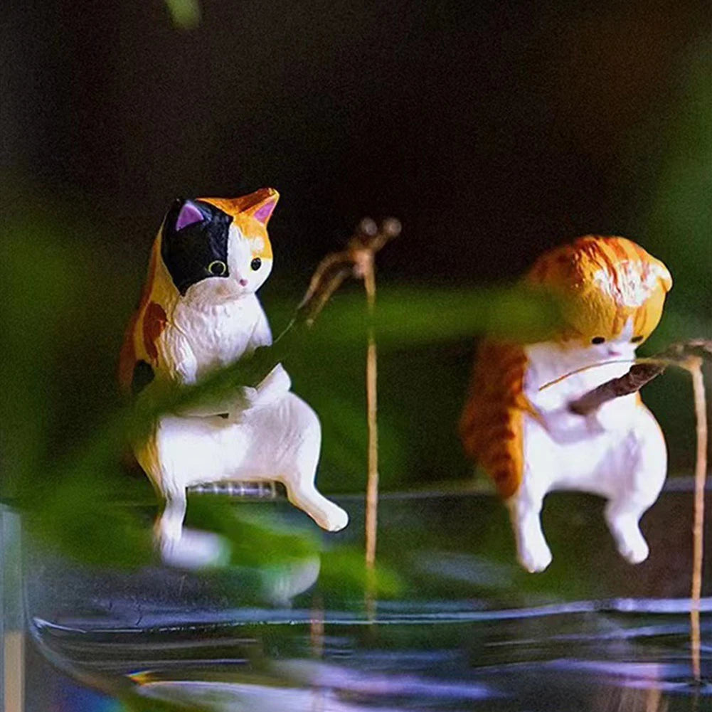 Two cute, hand-painted cat figurines in calico and ginger patterns, perched on an aquarium edge, holding fishing rods.
