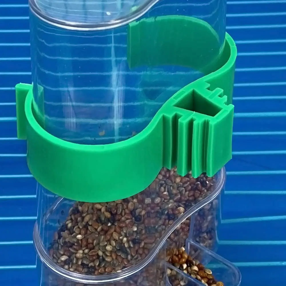 Clear plastic bird seed feeder with a bright green mounting clip, filled with mixed seeds against a blue grid backdrop.