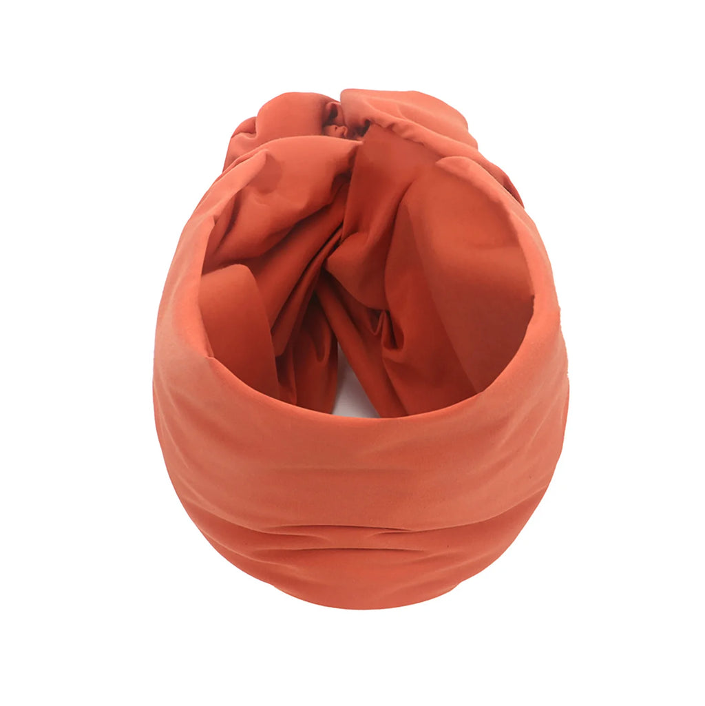 A rust-coloured vintage-style turban hat featuring a soft, knotted design with pleated detailing.