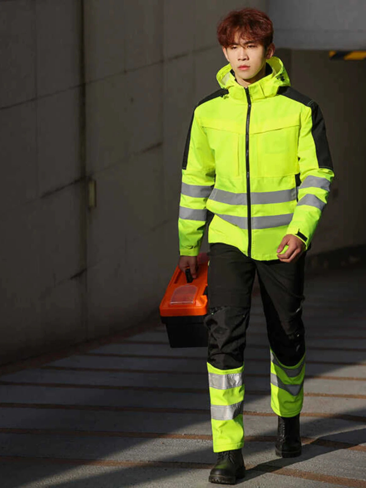 Worker wearing a yellow and black high-visibility waterproof jacket and trousers set with reflective tape strips.