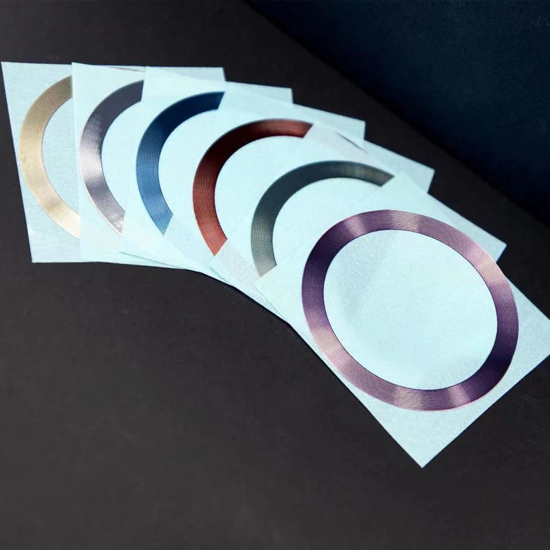 Set of six adhesive ring stickers in assorted metallic colours, arranged in a fan on light blue backing paper.
