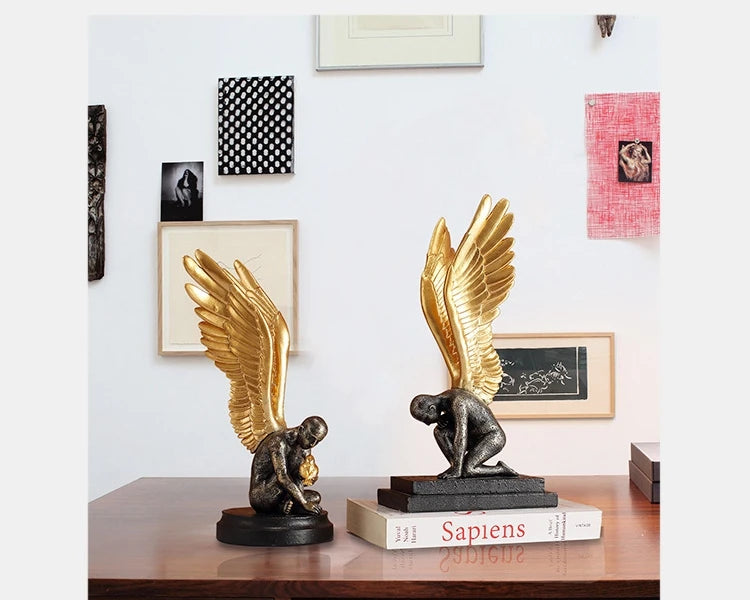 Two decorative statues of kneeling figures with large, ornate gold wings, set on black rectangular bases.
