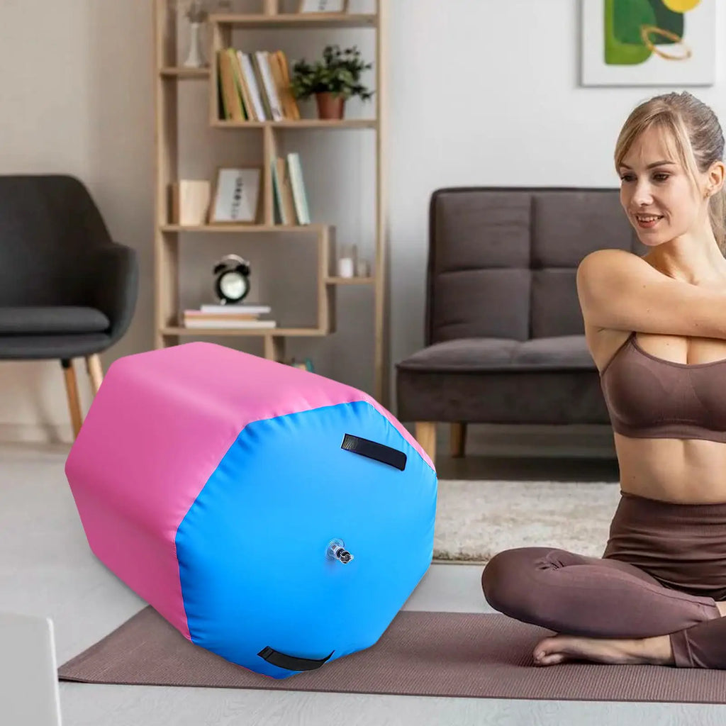Pink and blue inflatable gymnastic air roller barrel with black carry handles and an inflation valve in a living room.