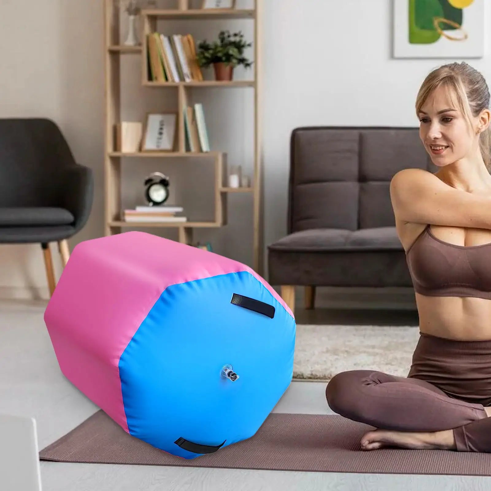 Pink and blue inflatable gymnastic air roller barrel with black carry handles and an inflation valve in a living room.