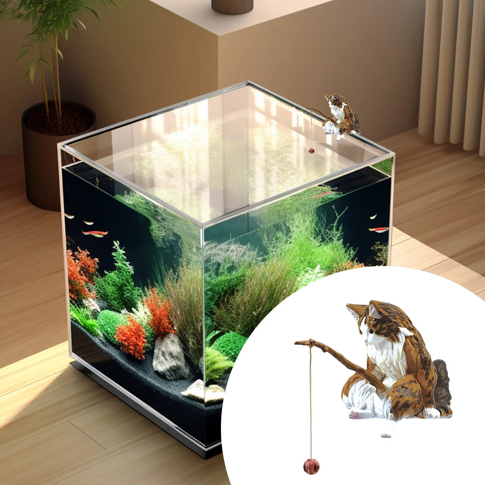 A brown and white tabby cat ornament, fishing with a small rod, perched on the edge of a glass aquarium.