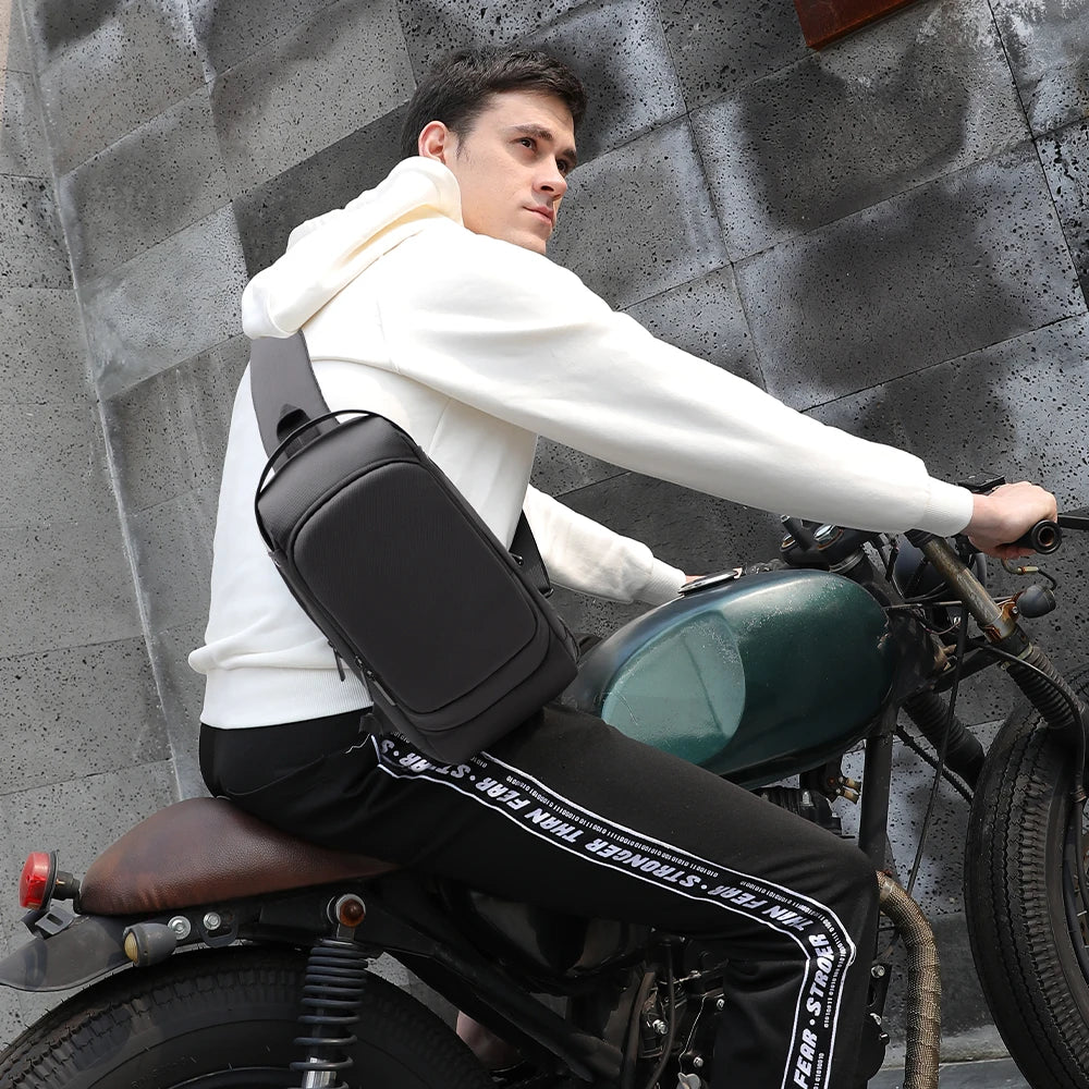 A man on a motorbike wearing a sleek, black waterproof crossbody sling bag with a built-in USB charging port.