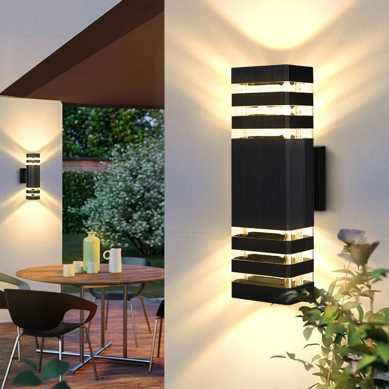 Modern black rectangular outdoor wall light casting warm upward and downward beams on a patio wall.