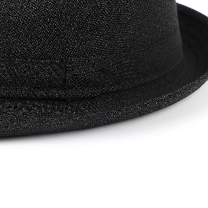 Close-up of a classic black felt-style fedora hat with a narrow brim and matching fabric band detail.
