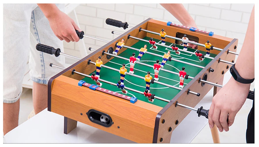Tabletop foosball game with wood-effect finish, green pitch, sliding scorers, and colourful player figurines.